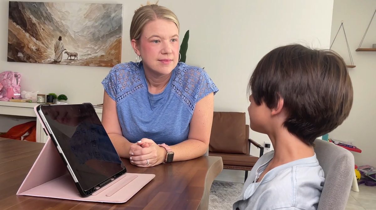 A mother and her son talking across the table, a tablet set up beside them