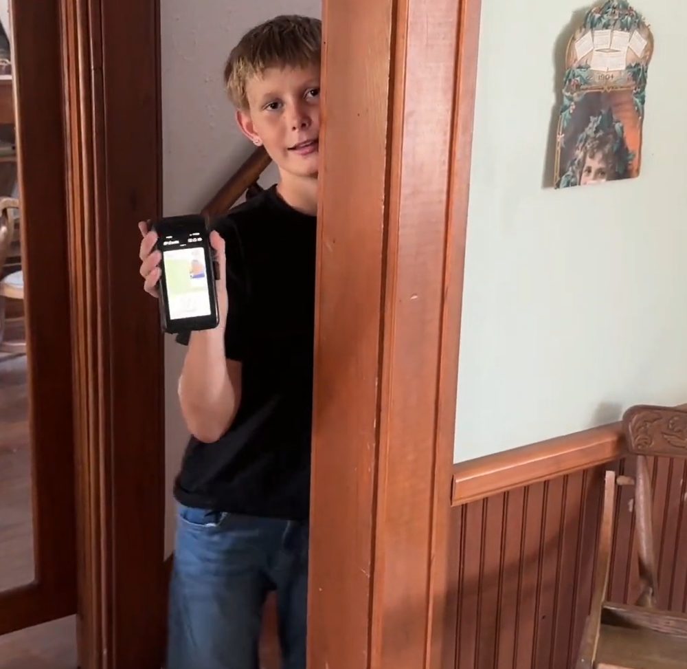 A Homeschool Pro student in a doorway, holding up his phone to show his digital student ID
